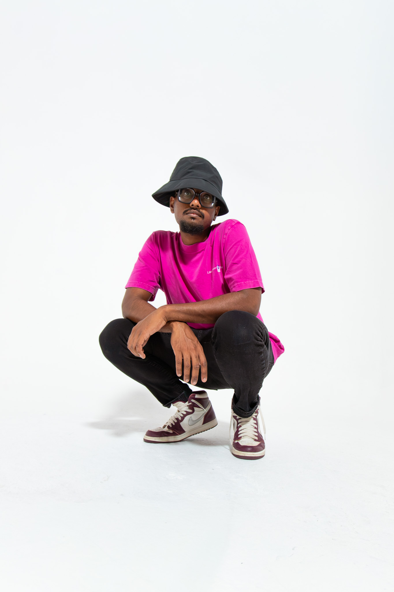 Crouching in a pink tee and bucket hat on a white cyclorama